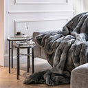 Stylish interior in subtle gray tones featuring luxurious home decor elements that exude comfort and design.  Ash-colored furry throw accentuates the refined ambiance, while a comfortable sofa surrounded by designer cushions and modern accents creates an inviting, cozy space. Minimalist decor paired with exclusive accent pieces and a carefully curated arrangement ensures every detail radiates sophisticated elegance, perfect for those who appreciate refined comfort and innovative design.