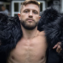 A man sits comfortably, wrapped in an exclusive black throw crafted from long-pile faux fur. The fabric radiates elegance, while its exceptional softness provides maximum comfort. An ideal choice for stylish, minimalist interiors – blending modern chic with a cozy atmosphere.