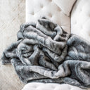 Luxurious home decor elements that exude comfort, design, and elegance. A ash-colored furry throw accentuates the refined ambiance, while a comfortable sofa surrounded by designer cushions and modern accents creates an inviting, cozy space. Minimalist decor paired with exclusive accent pieces and a carefully curated arrangement ensures every detail radiates sophisticated elegance, perfect for those who appreciate refined comfort and innovative design.